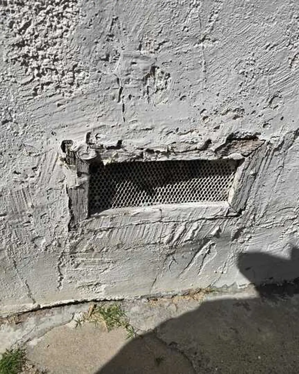 Damaged exterior wall surface surrounding a low rectangular vent